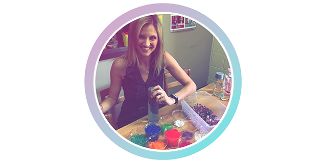 A woman is sitting at a table with a bottle of paint.