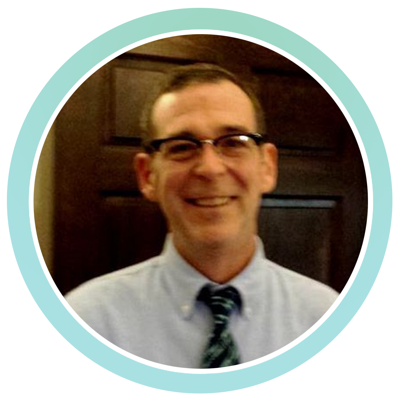 A man wearing glasses and a blue shirt is smiling.