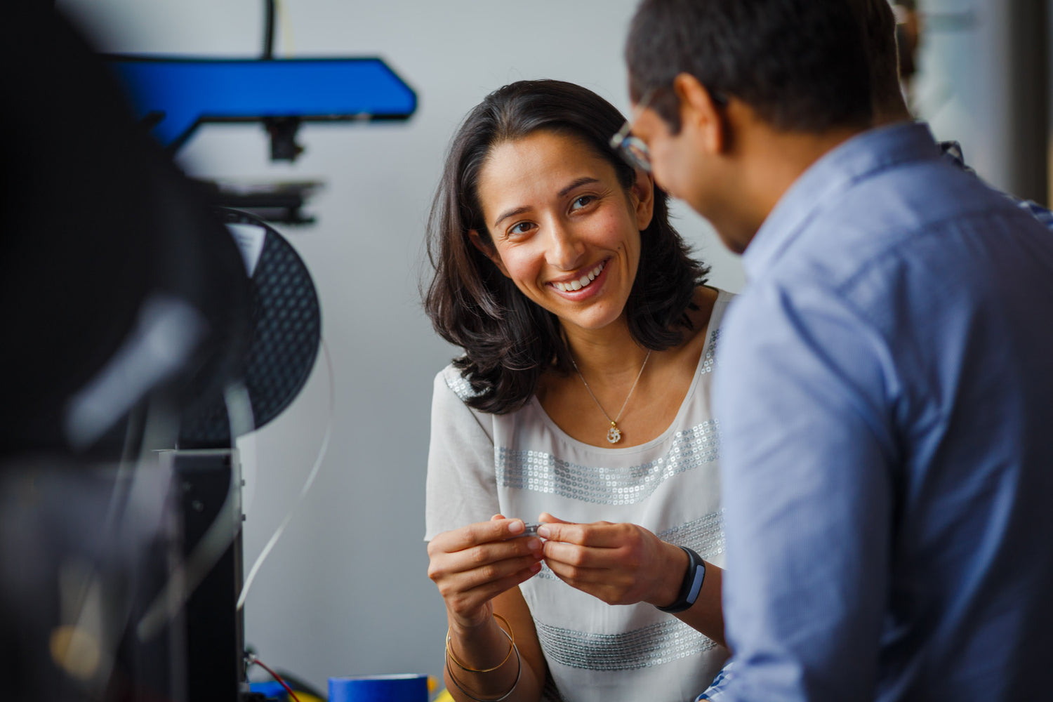 A man and woman in an office looking at a 3d printer.