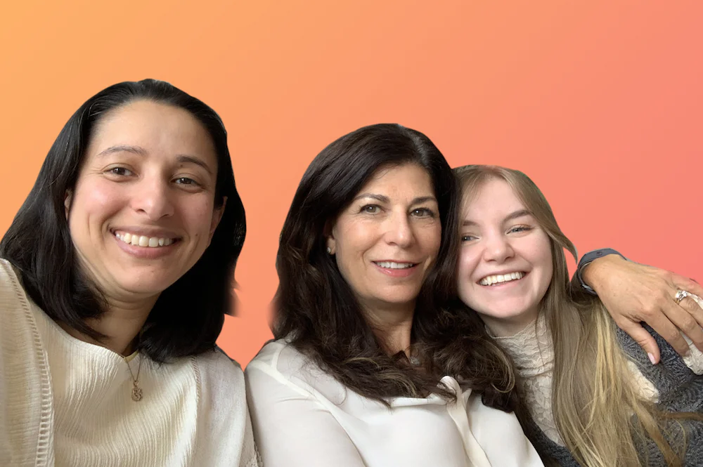Three women posing for a photo with an orange background.